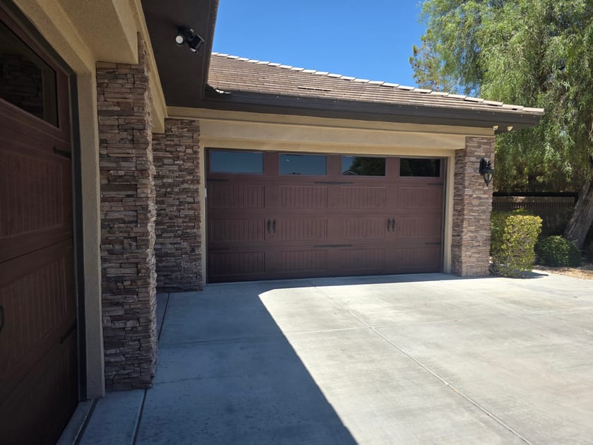 A brown double garage door framed by stone faced columns, with a camera mounted above the opening.