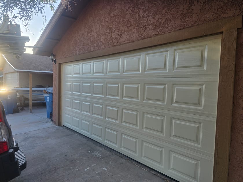 A cream coloured double garage door with short raised panels on a stucco home.