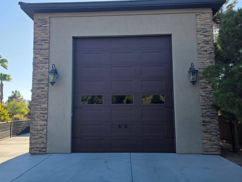 A tall garage door on a light stucco building with a coach lamp on each side of the opening.