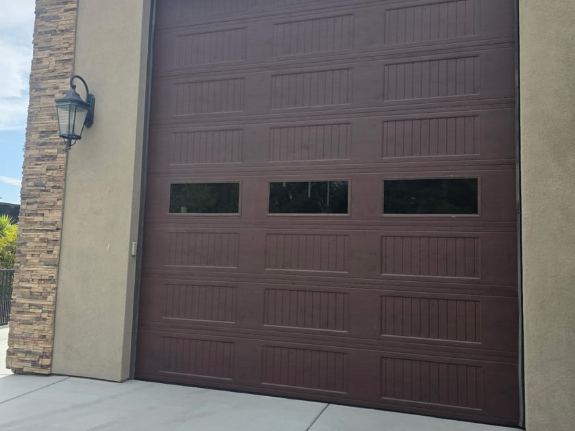 A tall brown garage door with a row of windows across the upper panel, sized for a high bay.