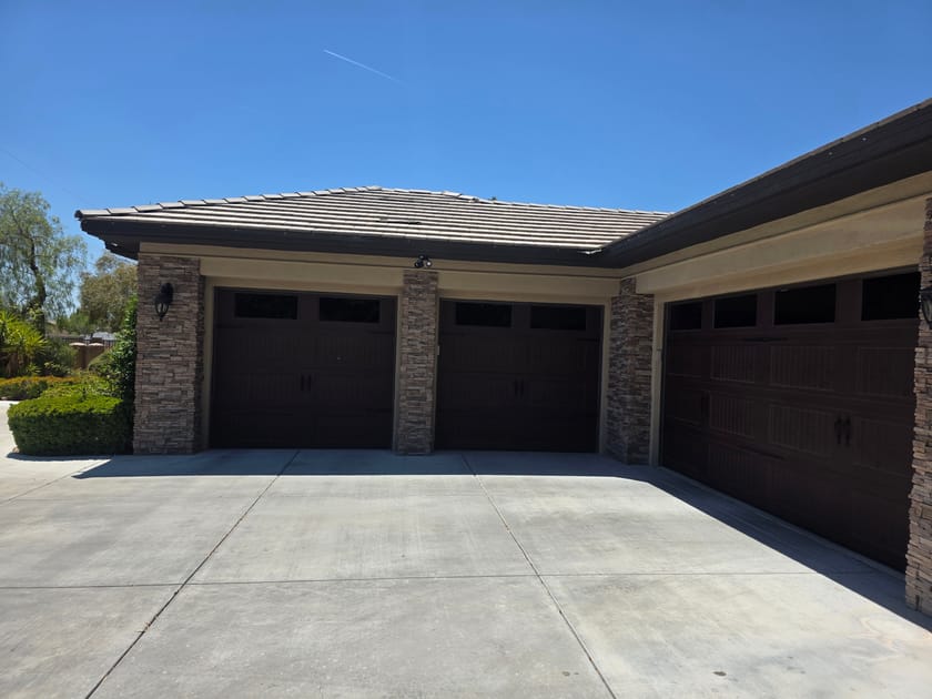 Three brown garage doors with stone faced columns between them on a single storey home.
