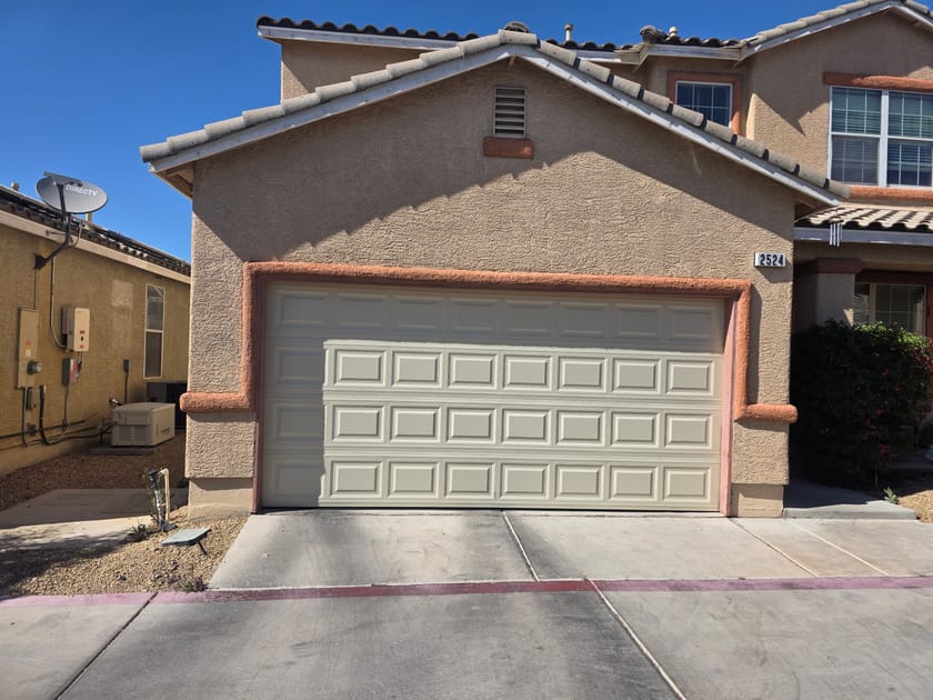 A cream garage door on a tan stucco house with a tile roof and a wide concrete driveway.