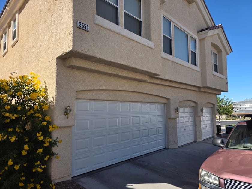 A two storey stucco home with a white double garage door and a single garage door beside it.