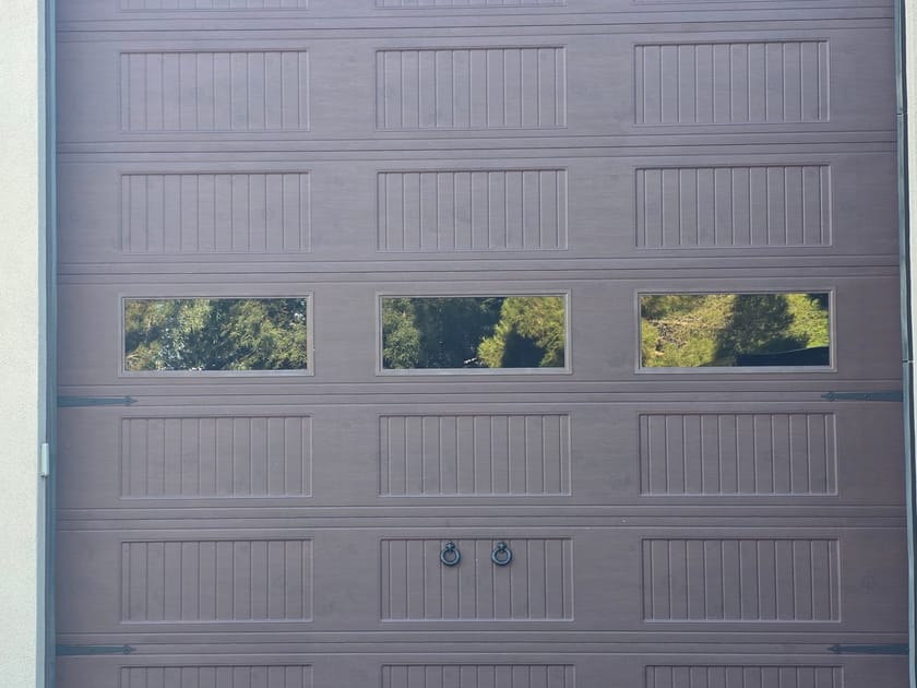 A brown garage door with a row of frosted windows set into the upper panel.