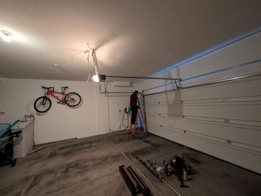 A ceiling-mounted garage door opener and its rail above a closed door in a Las Vegas garage, with a Prestige Garage Door Services technician on a ladder at the track.