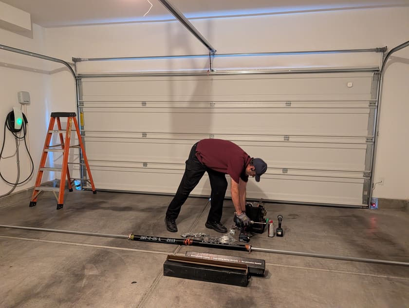 Prestige Garage Door Services technician at work in a Las Vegas garage, with a replacement torsion spring, shaft and cable drums laid out on the floor.