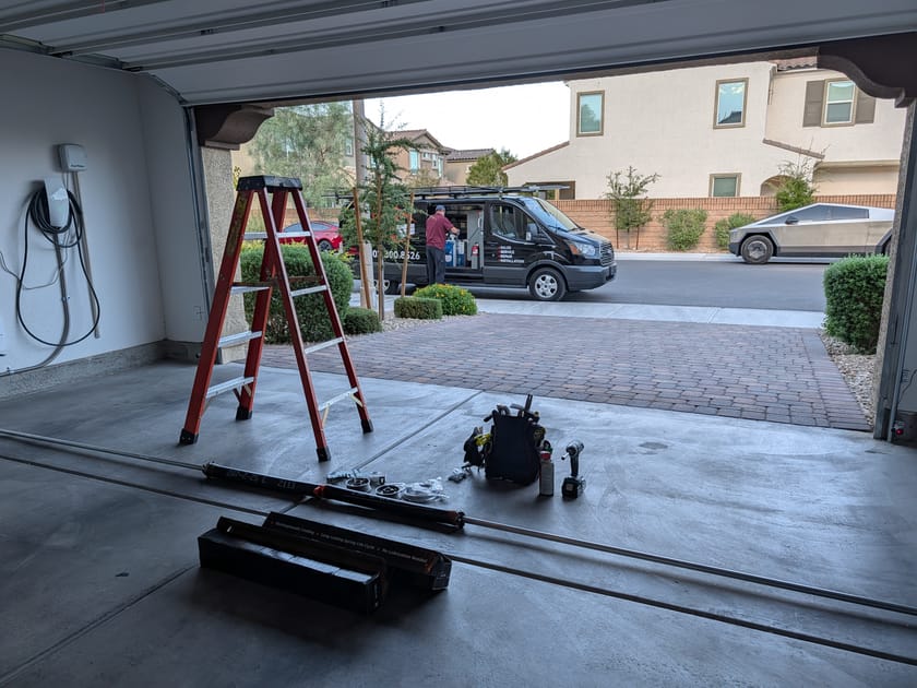 An open garage with a stepladder and garage door opener parts laid out on the floor ready for installation.