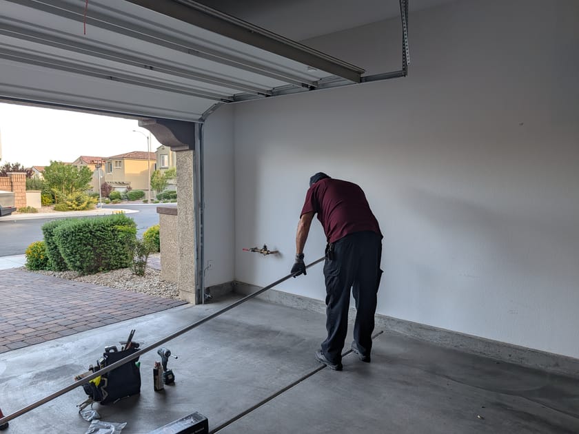 A technician working along the floor at the bottom track of an open garage door.