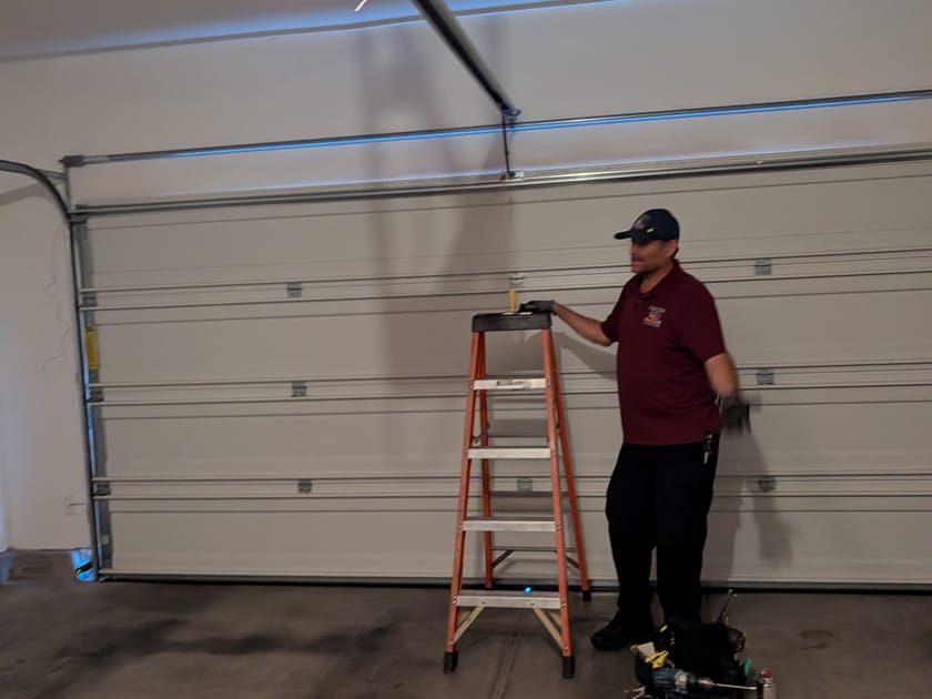 A technician standing beside a stepladder under a newly fitted and lit garage door opener.