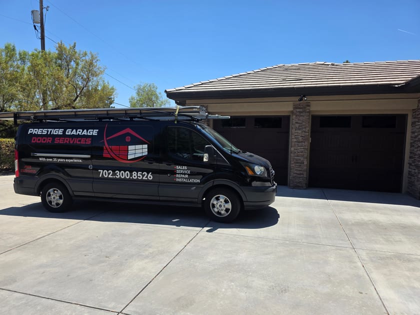 The Prestige Garage Door Services van parked on a driveway in front of a home with three brown garage doors.