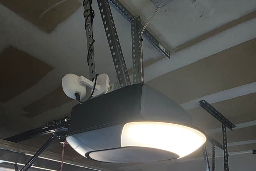 A garage door opener mounted on a residential garage ceiling, with its rail and hanging brackets.