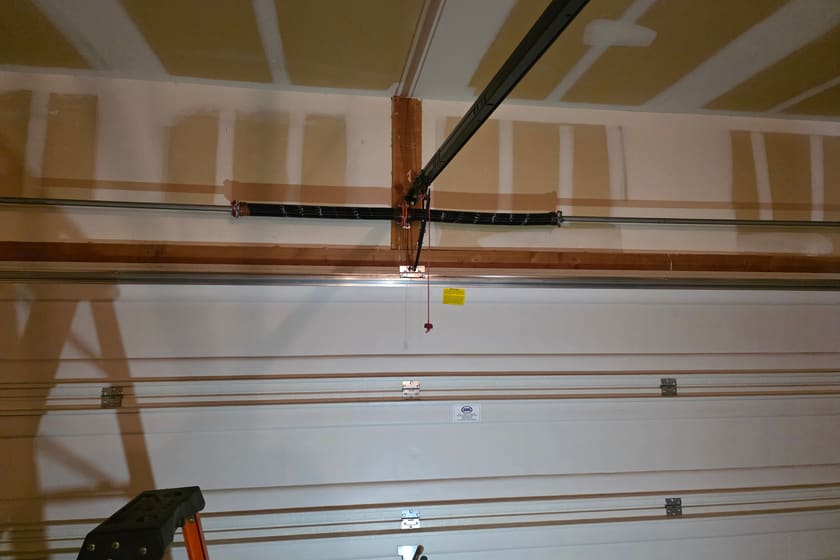 A torsion spring on its shaft above a closed garage door, with the opener rail running alongside it.